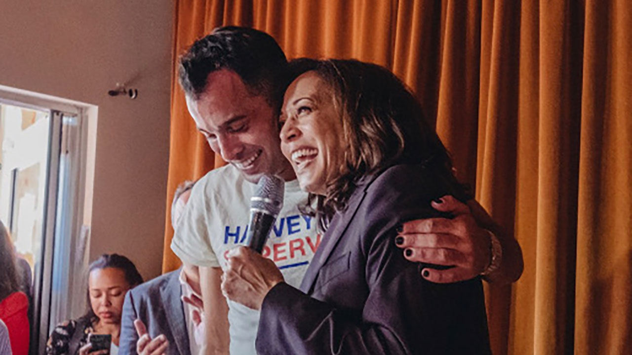 Harris and Yekutiel stand together on a stage, hugging sideways